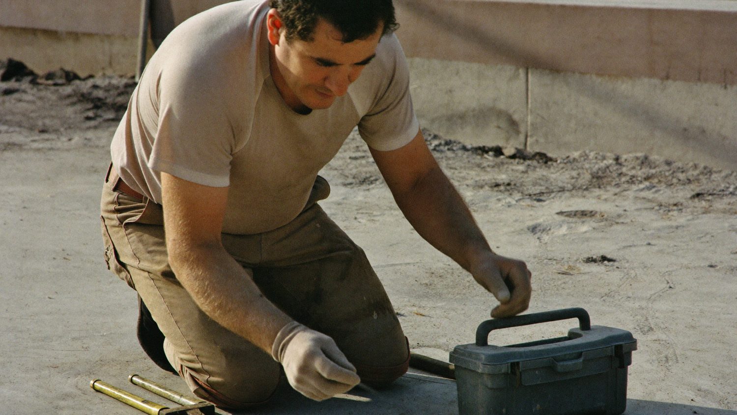 An independent contractor kneeling on a job site, working with his hands